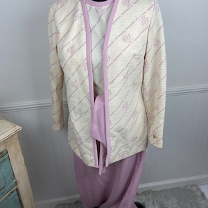 May include: A three-piece suit in a cream and pink color scheme. The jacket has a floral pattern and a pink trim. The skirt and top are solid pink.