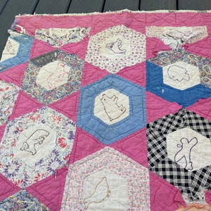 May include: A pink and blue patchwork quilt with a variety of floral patterns. The quilt is hand-stitched and features embroidered animals, including bears, birds, and a squirrel.