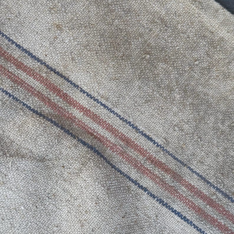 May include: Close-up of a piece of off-white fabric with two red stripes and one blue stripe running diagonally across the surface.