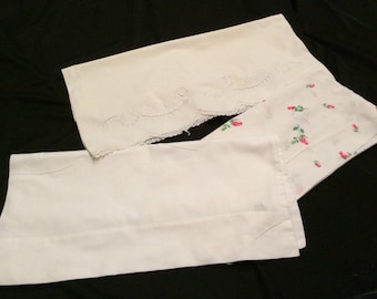 May include: Three white cotton pillowcases, one with a lace trim and floral embroidery, one with a floral print, and one plain.