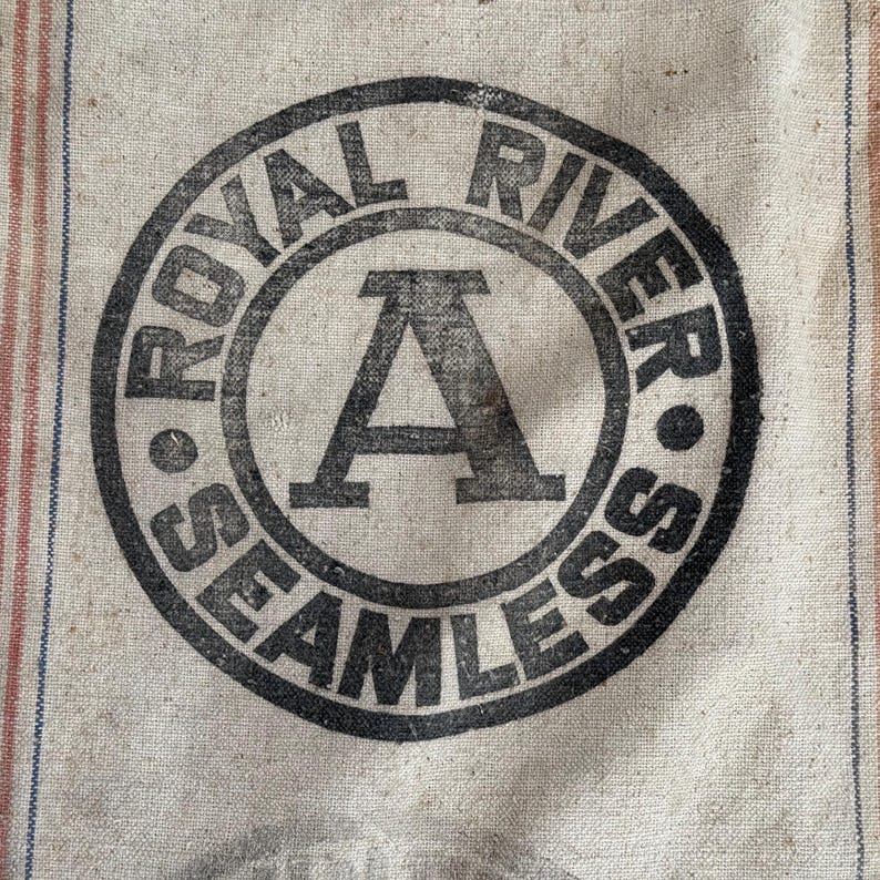 May include: A vintage burlap sack with a black and white circular logo that reads "Royal River Seamless" with a large letter "A" in the center.