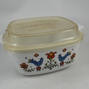 May include: A white rectangular casserole dish with integrated side handles and a clear plastic lid. The exterior features a colourful graphic print of two blue birds, a central orange tulip, and various small red and yellow flowers on green stems.