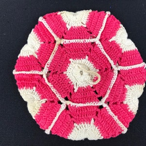 May include: A pink and white crocheted pot holder with a scalloped edge.
