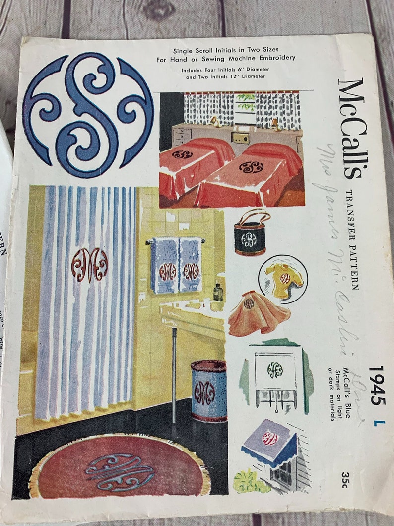 May include: McCall's Transfer Pattern 1945 L, a blue transfer pattern for embroidery. The pattern includes four 6-inch and two 12-inch scroll initials. The pattern is shown on a variety of household items, including towels, a shower curtain, a rug, and a wastebasket.