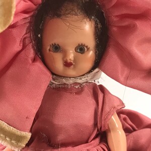 May include: A vintage doll with a pink dress and a large pink flower hat. The doll has dark hair, painted eyes, and a painted smile.