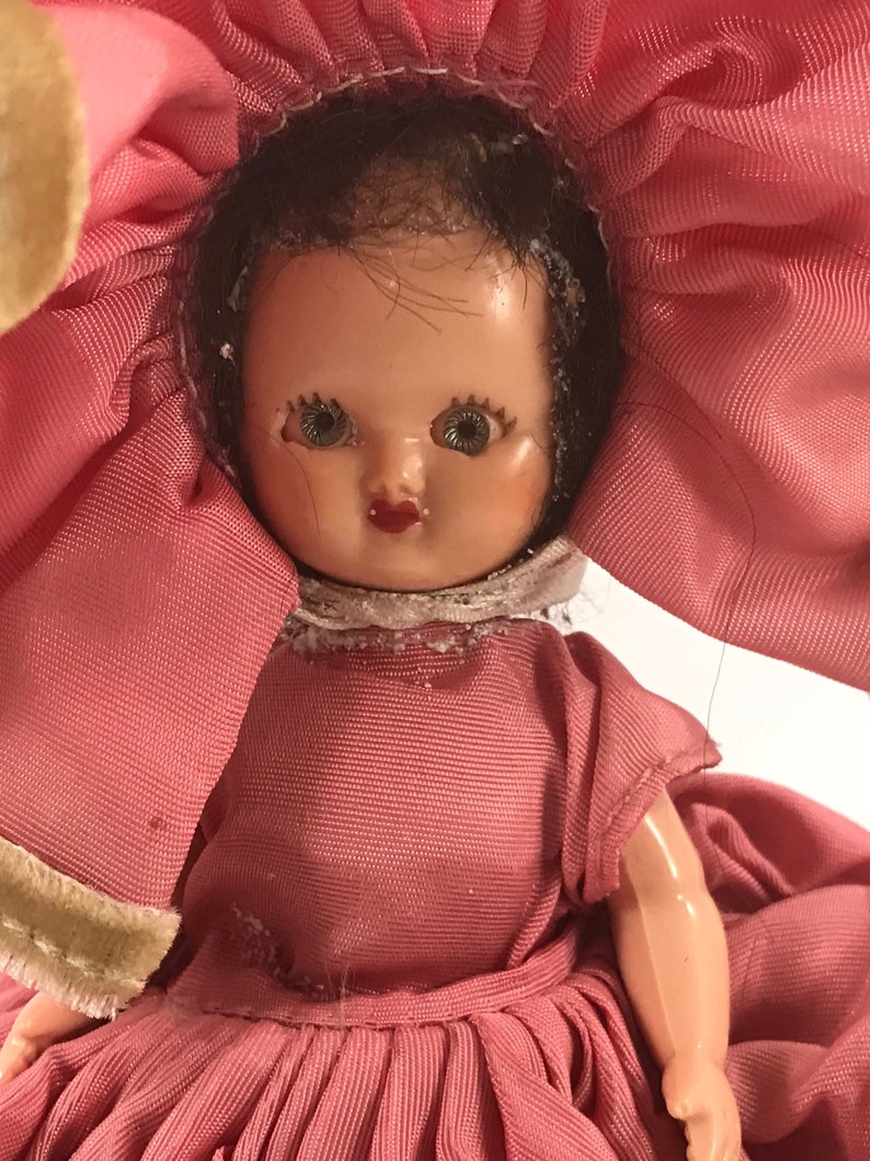 May include: A vintage doll with a pink dress and a large pink flower hat. The doll has dark hair, painted eyes, and a painted smile.