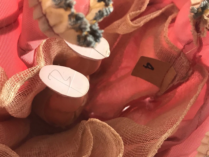 May include: Close-up of a pink dress with a tulle overlay. The dress has a number "2" written on one leg and a number "4" written on the other leg.