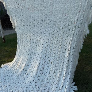 Pode incluir: Cobertor branco de crochê com um padrão de diamante e franjas. O cobertor é feito de um material macio e leve, perfeito para adicionar um toque de elegância a qualquer cômodo.