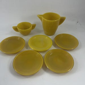 May include: A vintage yellow ceramic tea set, including a creamer, a cup, and six saucers. The set has a classic design with a smooth, glossy finish. The saucers are approximately 5 inches in diameter.