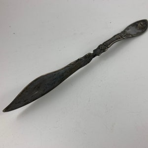 Puede incluir: Un cuchillo de mantequilla de plata con un mango adornado con un diseño de uva. La hoja está ligeramente deslustrada.