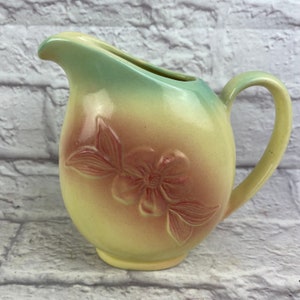 May include: A vintage ceramic pitcher with a floral design. The pitcher is yellow with a green and pink ombre effect. The floral design is in shades of pink and features a large flower with two leaves.