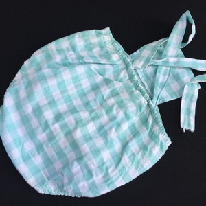 May include: A green and white gingham baby onesie with a matching strap. The onesie has a ruffled neckline and a gathered skirt.