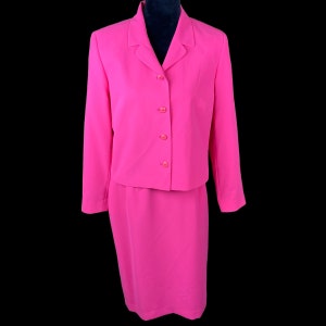 Pode incluir: Um conjunto de saia rosa choque com uma jaqueta curta e uma saia até o joelho. A jaqueta tem um fecho de botões na frente e uma gola.