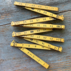 May include: A set of ten yellow folding rulers with black markings. The rulers are made of wood and have a metal end cap. The rulers are all different lengths, ranging from 6 inches to 36 inches. The rulers are all in good condition and have been well-used.