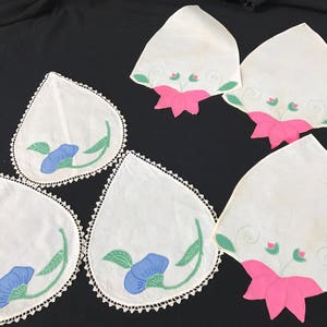 Può includere: Cinque tovagliette all'uncinetto bianche con ricami floreali. Le tovagliette presentano fiori blu e verdi con accenti rosa.