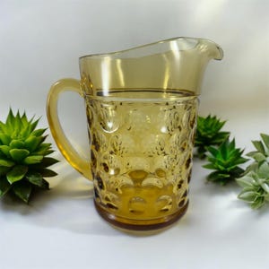 May include: Amber glass pitcher with a textured, bubble-like design. The pitcher has a wide mouth and a handle.