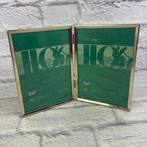 May include: A gold-toned metal picture frame with two 5x7 inch openings. The frame is hinged in the middle and can be folded to display two photos.