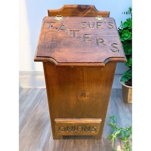 Könnte beinhalten: Eine Holzkiste mit Scharnierdeckel und unterem Fach. Der Deckel ist mit "SUE'S TATERS" graviert. Das untere Fach ist mit "ONIONS" beschriftet. Die Kiste ist aus gebeiztem Holz gefertigt.