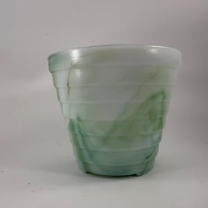 Op de afbeelding: Een wit en groen gezwierde glazen plantenbak met een geribbeld ontwerp. De plantenbak heeft een cilindrische vorm met een iets uitlopende bovenkant en een reeks horizontale ribbels. De groene wervelingen voegen een decoratief tintje toe.
