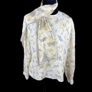May include: A vintage floral blouse and scarf set. The blouse is white with a pattern of large yellow flowers and gray leaves. The scarf is draped around the neck and has a matching floral pattern with a gray border. The blouse has long sleeves.