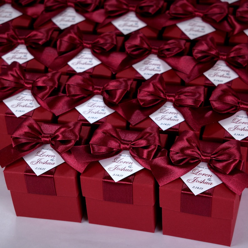 K&ouml;nnte beinhalten: Eine gro&szlig;e Gruppe kleiner, quadratischer Geschenkboxen in Burgunderrot mit wei&szlig;en Satinb&auml;ndern und personalisierten Etiketten mit der Aufschrift "Vielen Dank Loren & Joshua 2.14.21".