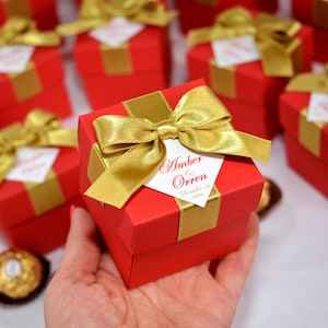 Può includere: Scatole regalo rosse con nastro dorato e un'etichetta bianca che dice "Amber & Orren 19 dicembre 2020".