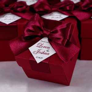 K&ouml;nnte beinhalten: Bordeauxfarbene Geschenkboxen mit einer Schleife aus Satinband und einem wei&szlig;en Etikett mit der Aufschrift "Danke Loren & Joshua 2.14.21".
