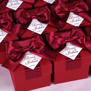 K&ouml;nnte beinhalten: Weinrote Geschenkboxen mit wei&szlig;en Satinb&auml;ndern und personalisierten Etiketten mit der Aufschrift "Danke Loren & Joshua 2.14.21".