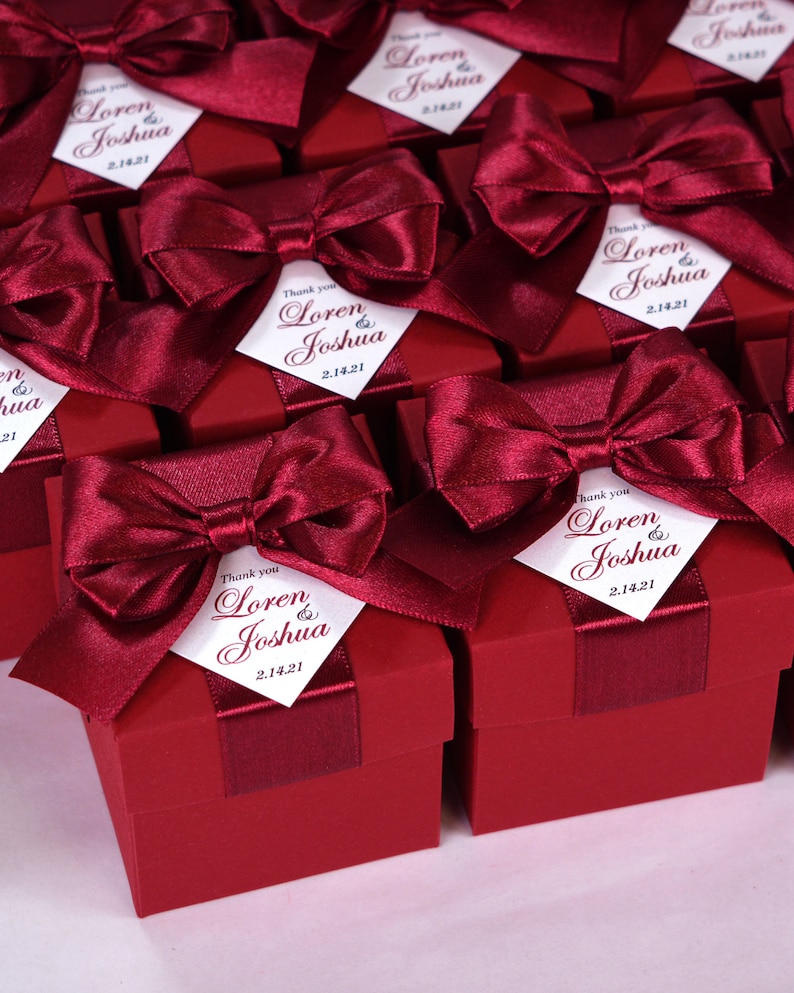 K&ouml;nnte beinhalten: Weinrote Geschenkboxen mit wei&szlig;en Satinb&auml;ndern und personalisierten Etiketten mit der Aufschrift "Danke Loren & Joshua 2.14.21".