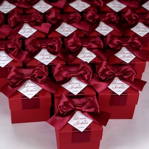 K&ouml;nnte beinhalten: Weinrote Geschenkboxen mit wei&szlig;en Satinb&auml;ndern und personalisierten Etiketten mit der Aufschrift "Danke Loren & Joshua 2.14.21".