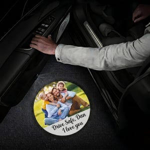 May include: A circular car floor mat with a family photograph and the text "Drive Safe, Dan I love you". The mat is positioned inside a car, near the open door.
