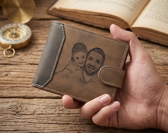 May include: A brown bi-fold wallet featuring a dark brown leather accent panel on the left side and a snap button closure. The front surface displays a laser-engraved portrait of a smiling adult and a child, with visible stitching along the edges.
