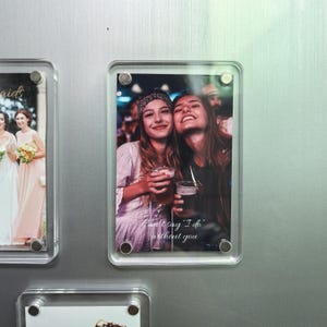 Könnte beinhalten: Ein klarer Acryl-Fotorahmen mit einem Bild von zwei lächelnden Frauen, die Getränke halten. Das Foto enthält den Text "Can't say 'I do' without you". Der Rahmen ist an einer silbernen Oberfläche befestigt.