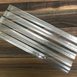 May include: Five clear plastic tubes, likely for holding small items, are arranged in a fan shape on a wooden surface.