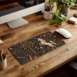 May include: A rectangular mouse pad featuring a detailed illustration of a white unicorn leaping through a dense forest scene. The design includes orange fruit trees, small rabbits, a bird, and colorful flowers set against a black background.