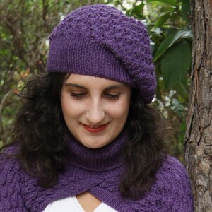 May include: A woman wearing a purple knitted hat and matching scarf. The hat is a beret style with a textured pattern. The scarf is a cowl style with a simple knit.