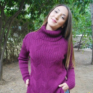 May include: A purple turtleneck sweater with a cable knit pattern. The sweater is long and has a relaxed fit.