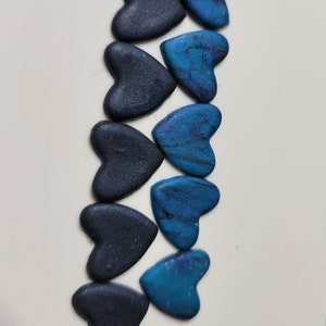 May include: A row of ten heart-shaped polymer clay charms in shades of blue and black. The charms are arranged in a gradient from dark blue to light blue.