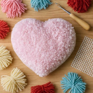 May include: A fluffy, light pink heart-shaped pom-pom surrounded by red, blue, and yellow pom-poms. A crochet hook and a white mesh grid are on a wooden surface. Ideal for crafting and DIY projects.