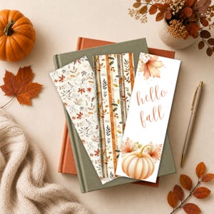 May include: Three rectangular bookmarks featuring autumn-themed designs. One displays a scattered leaf pattern, another has vertical stripes with foliage, and the third shows a pumpkin with the text hello fall in a script font.