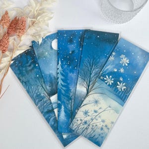 May include: Set of five blue watercolor bookmarks featuring wintery scenes with trees, stars, and a moon. The bookmarks are rectangular and have a white border.