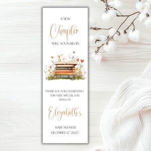 May include: A rectangular white bookmark featuring the text A NEW CHAPTER WILL SOON BEGIN, a watercolor illustration of a stack of books surrounded by wildflowers and hearts, followed by THANK YOU FOR CELEBRATING THIS VERY SPECIAL DAY WITH US!, Elizabeth's, BABY SHOWER, and DECEMBER 27, 2025.