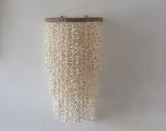 May include: A white shell mobile hanging from a wooden dowel. The mobile is made of many small white shells that are strung together in a cascading pattern.