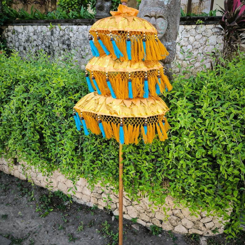 May include: A three-tiered yellow and blue decorative umbrella with tassels. The umbrella is made of fabric and has a wooden pole.