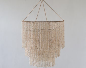 May include: A white shell chandelier with three tiers of cascading shells. The chandelier is suspended from a rope and has a simple, rustic design.