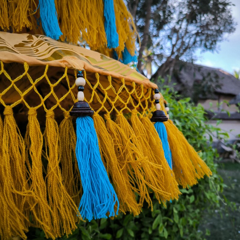 May include: A yellow and blue tassel garland with wooden beads. The garland is made of a net-like material and has a fringe of tassels.