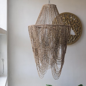Op de afbeelding: Een grote, bruine kralen kroonluchter met een uniek, cascade-ontwerp. De kroonluchter is gemaakt van natuurlijke materialen en heeft een rustieke, bohemian esthetiek.