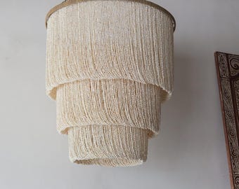May include: A white beaded chandelier with three tiers of cascading beads. The chandelier is hanging from a silver chain.