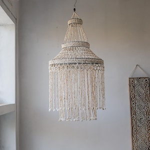 Puede incluir: Una gran lámpara de araña blanca de conchas con un diseño de niveles. La lámpara de araña está hecha de muchas conchas pequeñas que se ensartan juntas para crear un patrón delicado e intrincado.