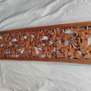 Può includere: Un'opera d'arte murale rettangolare in legno con un design floreale intagliato. Presenta dettagliati fiori di ibisco e foglie in una calda tonalità di legno naturale. Il pezzo è incorniciato e adatto all'arredamento della casa.